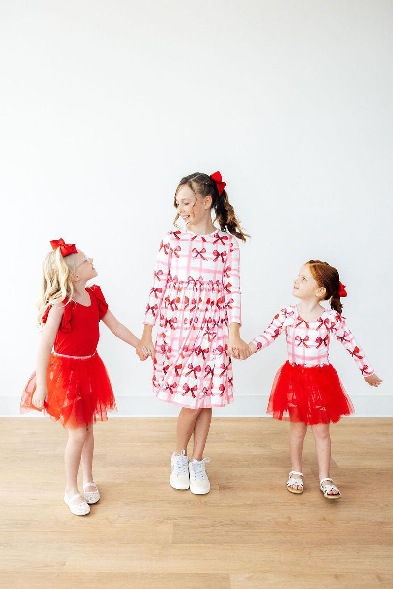 Three girls joyfully holding hands, dressed in coordinated outfits featuring the Bow La La Tutu Shorts and matching attire, embodying fun and playful style.