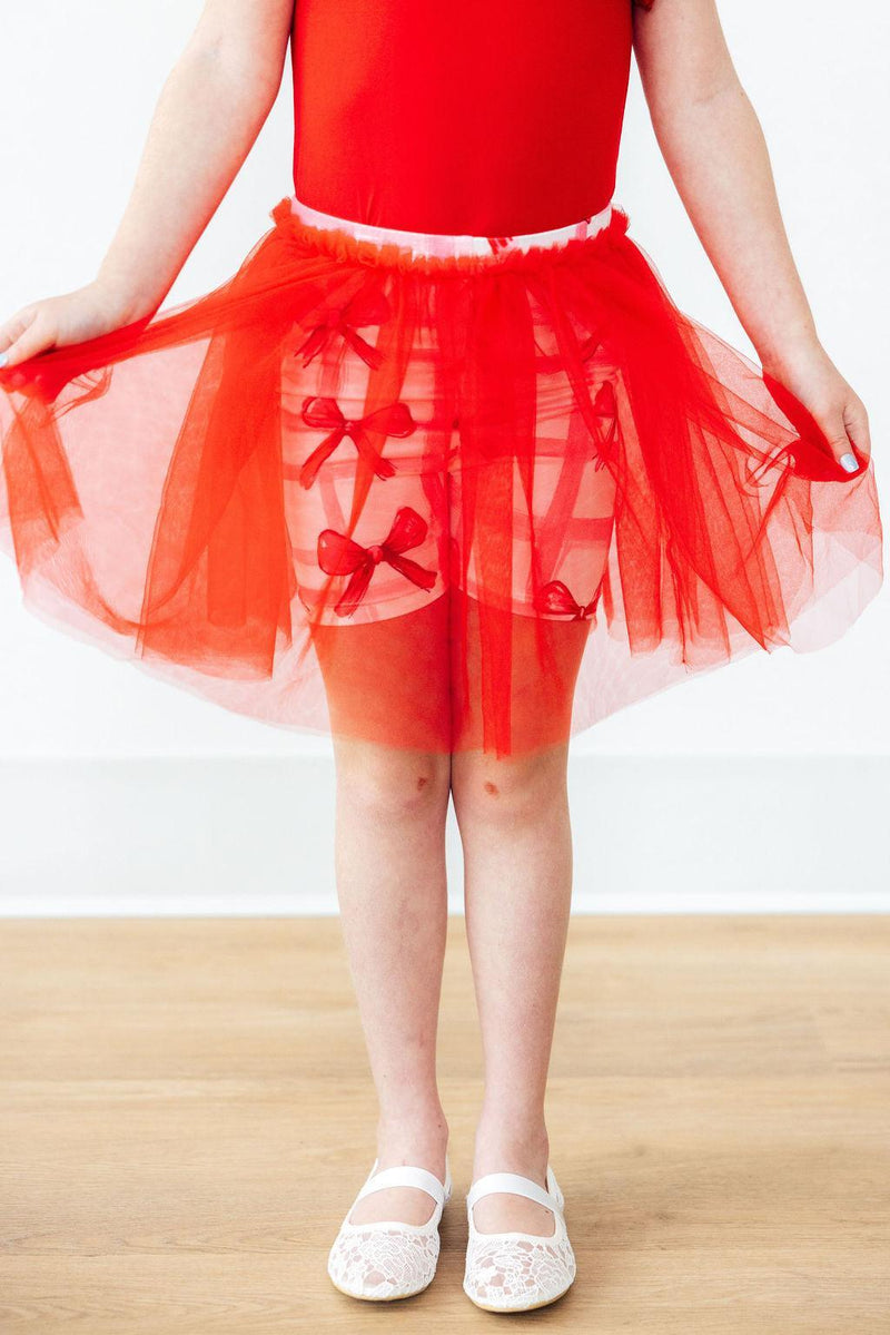 A little girl wearing the Bow La La Tutu Shorts in vibrant red, showcasing the adorable tutu and playful design, perfect for dancing and twirling.