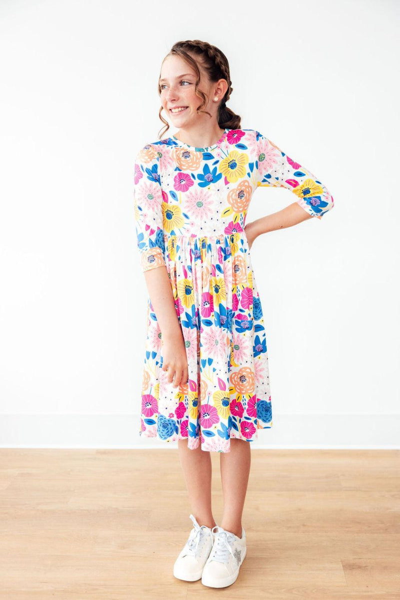A joyful girl posing in the 'Sunshine Floral' 3/4 Sleeve Pocket Floral Twirl Dress, highlighting the colorful floral pattern and twirl design, perfect for any occasion as a floral twirl dress.