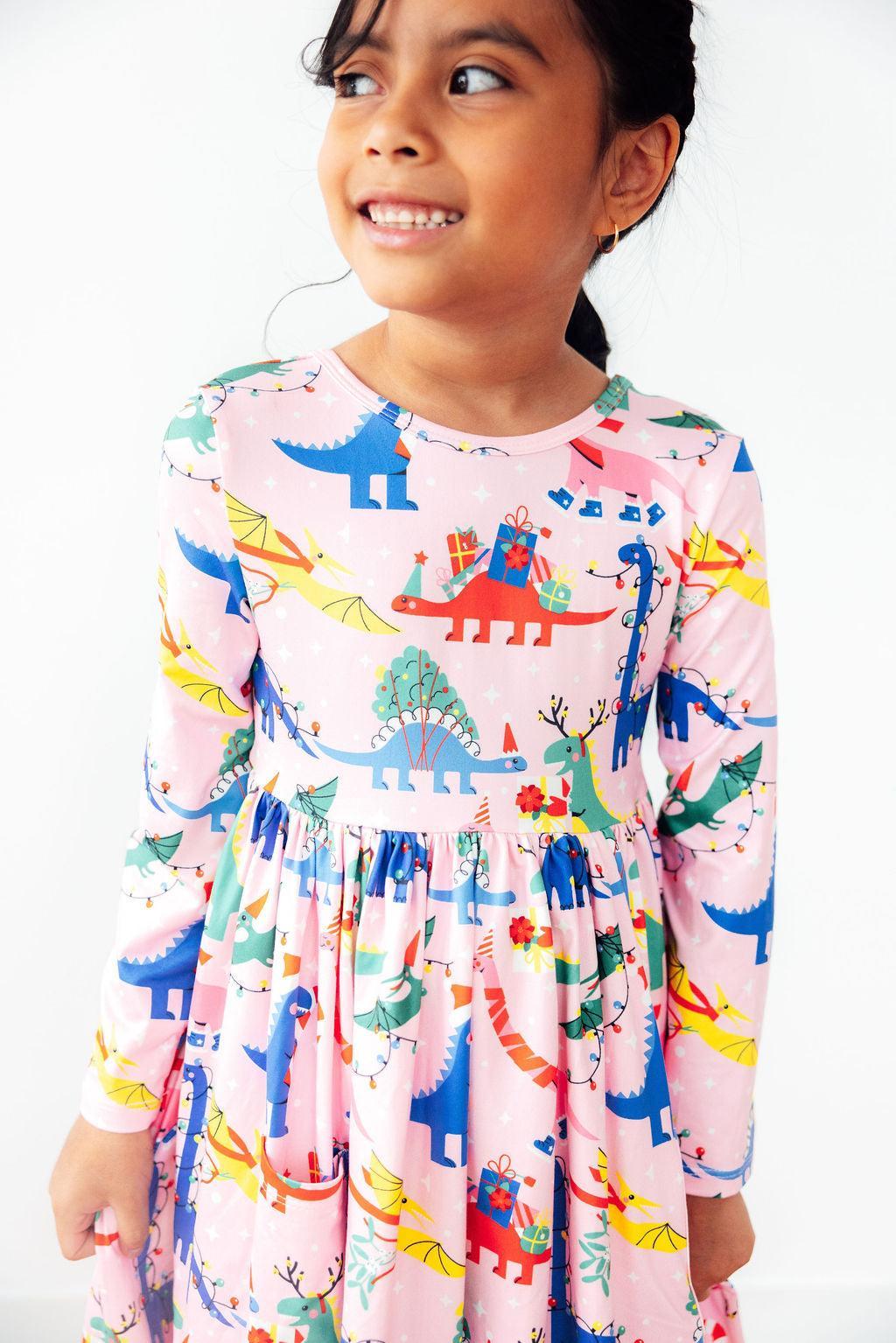 Adorable Jingle Saurus Long Sleeve Dress for Girls showcased by a smiling girl, featuring vibrant dinosaur prints, perfect for imaginative play and comfort. Ideal long sleeve dress for girls.
