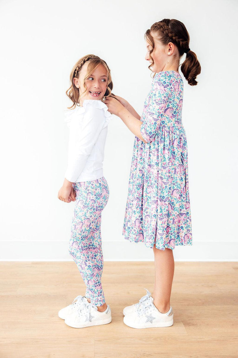 Two girls interacting, one wearing the Head in the Clouds 3/4 Sleeve Pocket Twirl Dress for Girls. This beautiful twirl dress for girls showcases a vibrant print, ideal for fun occasions.