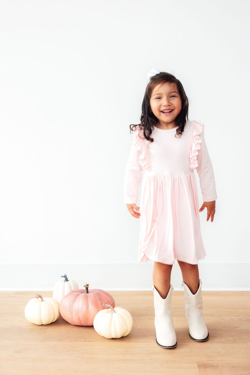 Charming little girl wearing a Petal Pink L/S Ruffle Twirl Dress by Mila & Rose®, standing among pumpkins and radiating joy, perfect for playful spins and smiles.