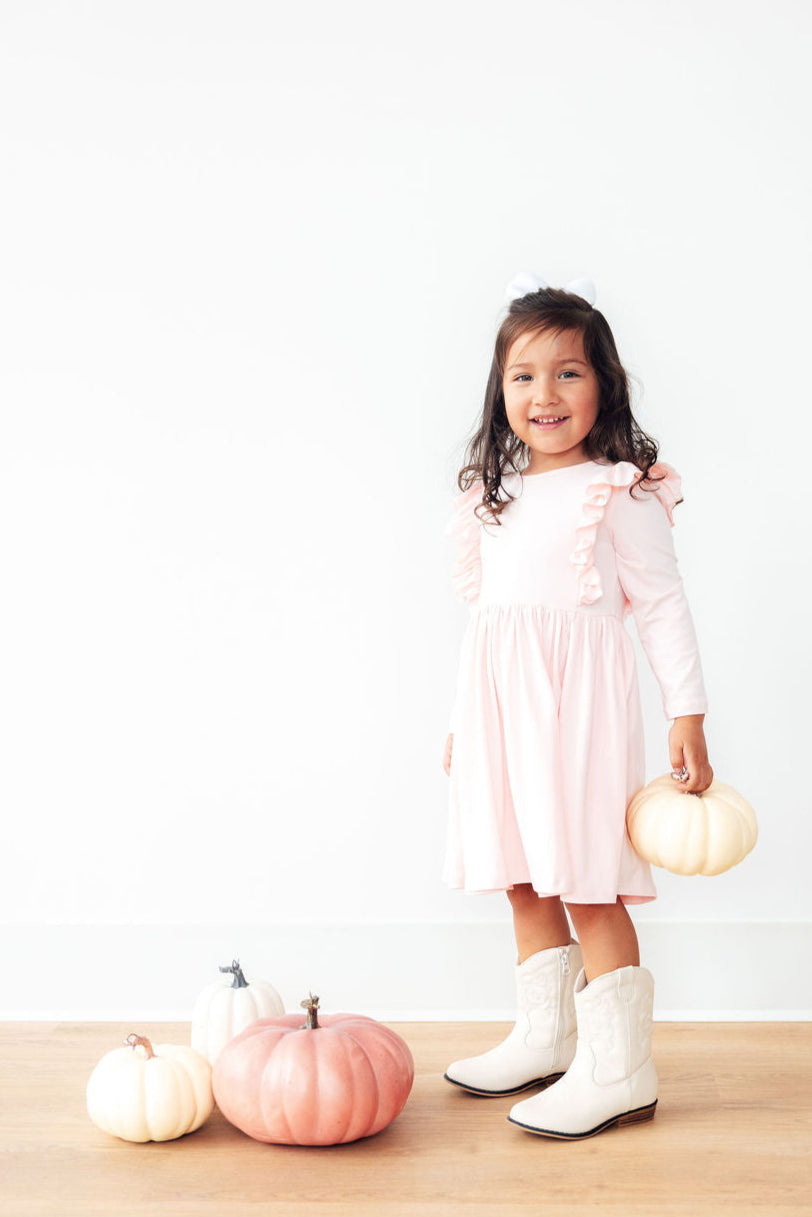 Adorable little girl in a Petal Pink L/S Ruffle Twirl Dress by Mila & Rose® smiling while holding a tiny pumpkin, perfect for twirling and fun fall occasions.