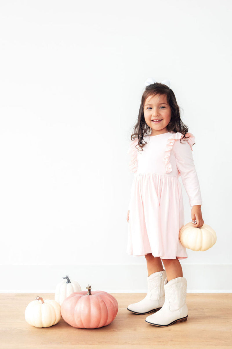 Adorable little girl in a Petal Pink L/S Ruffle Twirl Dress by Mila & Rose® smiling while holding a tiny pumpkin, perfect for twirling and fun fall occasions.
