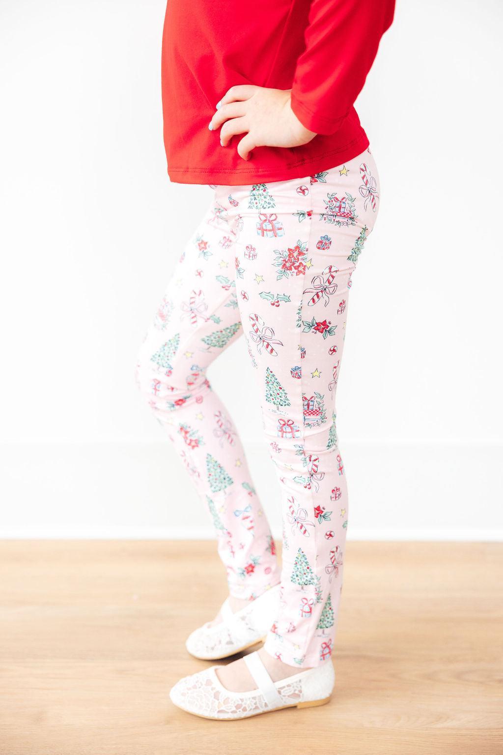 A child wearing pink Christmas leggings, featuring festive prints of trees and candy canes, paired with a red top, showcasing a stylish holiday outfit.