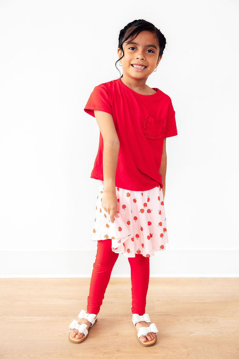 A girl cheerfully posing in An Apple a Day Twirl Skeggings for Girls, showcasing the stylish skirt and legging design perfect for active girls. The ideal choice of skeggings for girls.