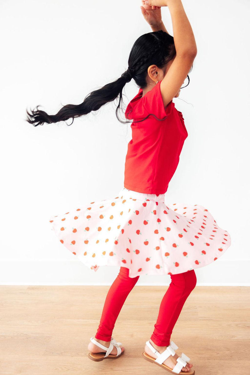 A girl playfully spinning in An Apple a Day Twirl Skeggings for Girls, displaying the twirl-worthy design that makes these skeggings for girls a favorite for active play.