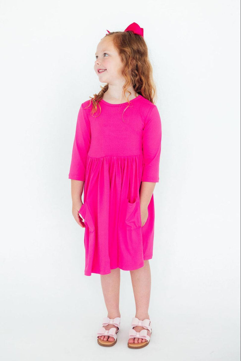 Delightful girl in a side profile view of a Hot Pink 3/4 Sleeve Pocket Twirl Dress, exuding joy and style with a playful smile.