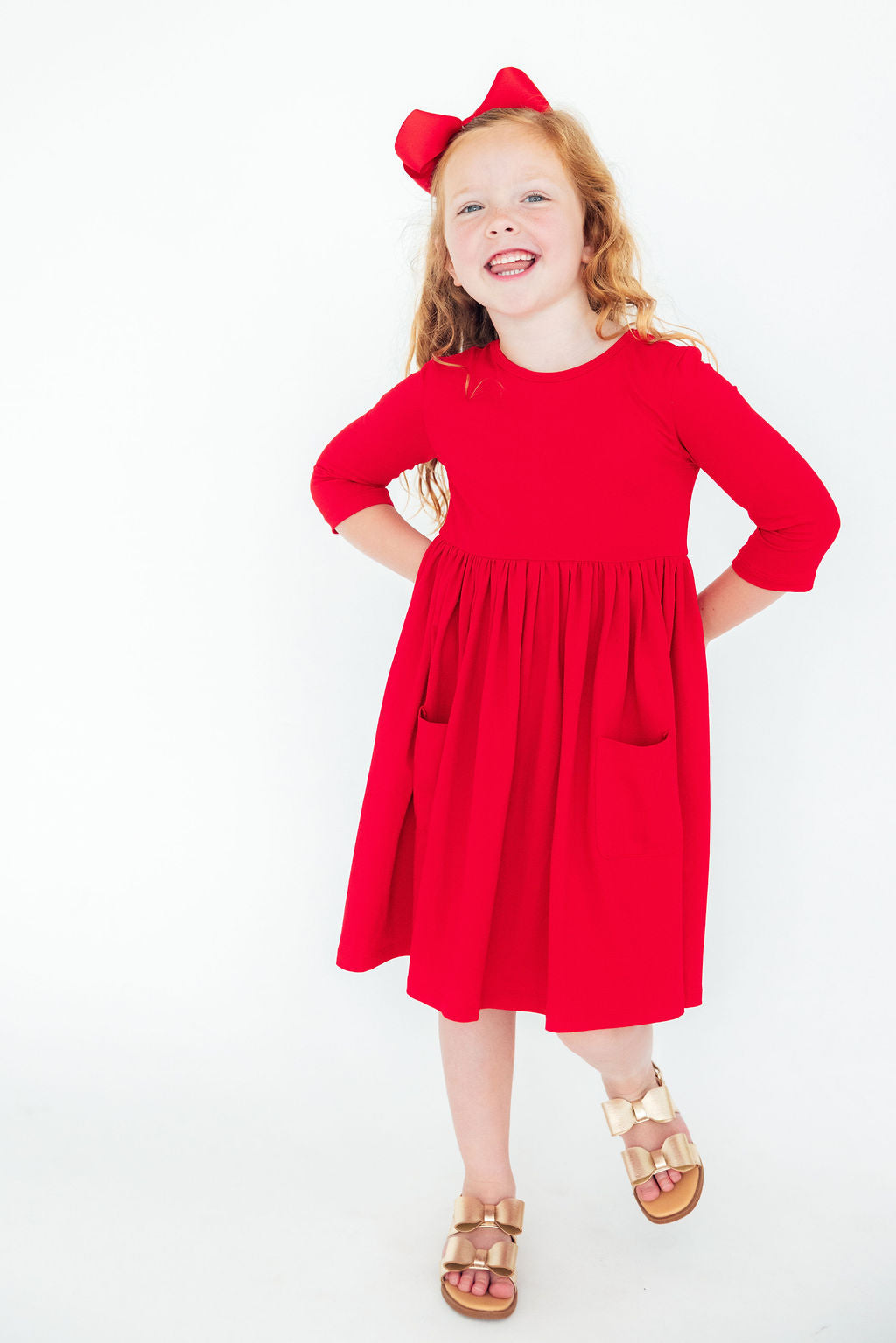 Joyful girl modeling the Red 3/4 Sleeve Pocket Twirl Dress by Mila & Rose, showcasing a playful design with pockets and a full-circle skirt.