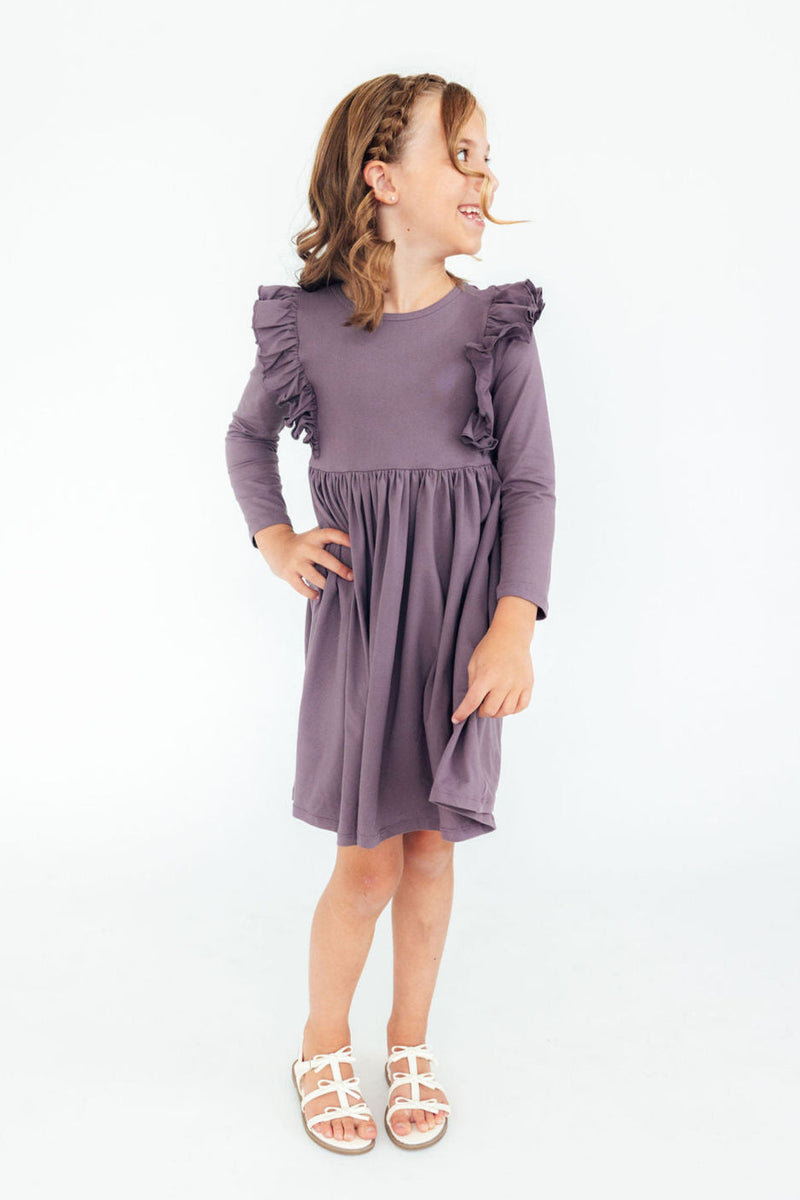 A joyful girl wearing the Vintage Violet Long Sleeve Ruffle Twirl Dress, displaying its stylish ruffles and twirl-friendly skirt.