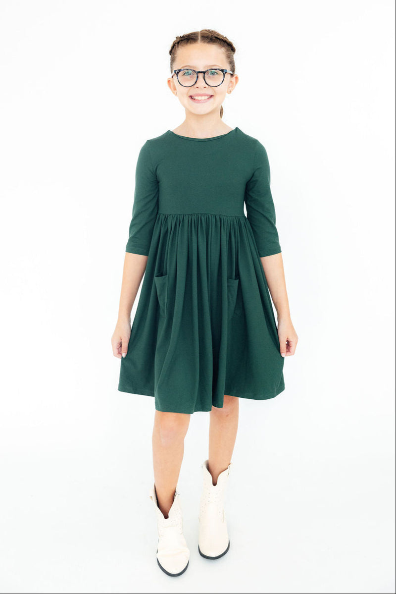 Happy child in the Spruce 3/4 Sleeve Pocket Twirl Dress, standing confidently with a big smile, highlighting the dress's pockets and charming design.