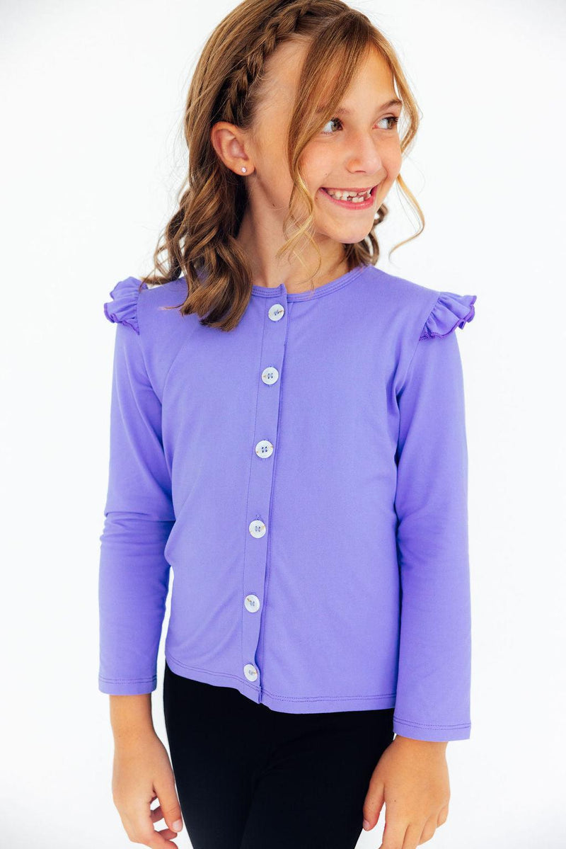 A stylish girl in a Periwinkle Ruffle Cardigan, turning playfully while highlighting its adorable ruffles and smooth fabric, perfect for twirls and adventures.