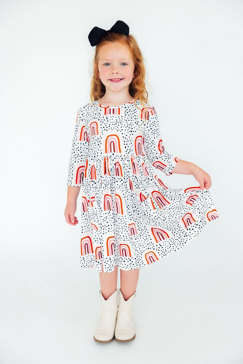 Delightful portrait of a girl in the Peach Rainbow 3/4 Sleeve Pocket Twirl Dress, twirling with joy, showcasing both style and a charming look.