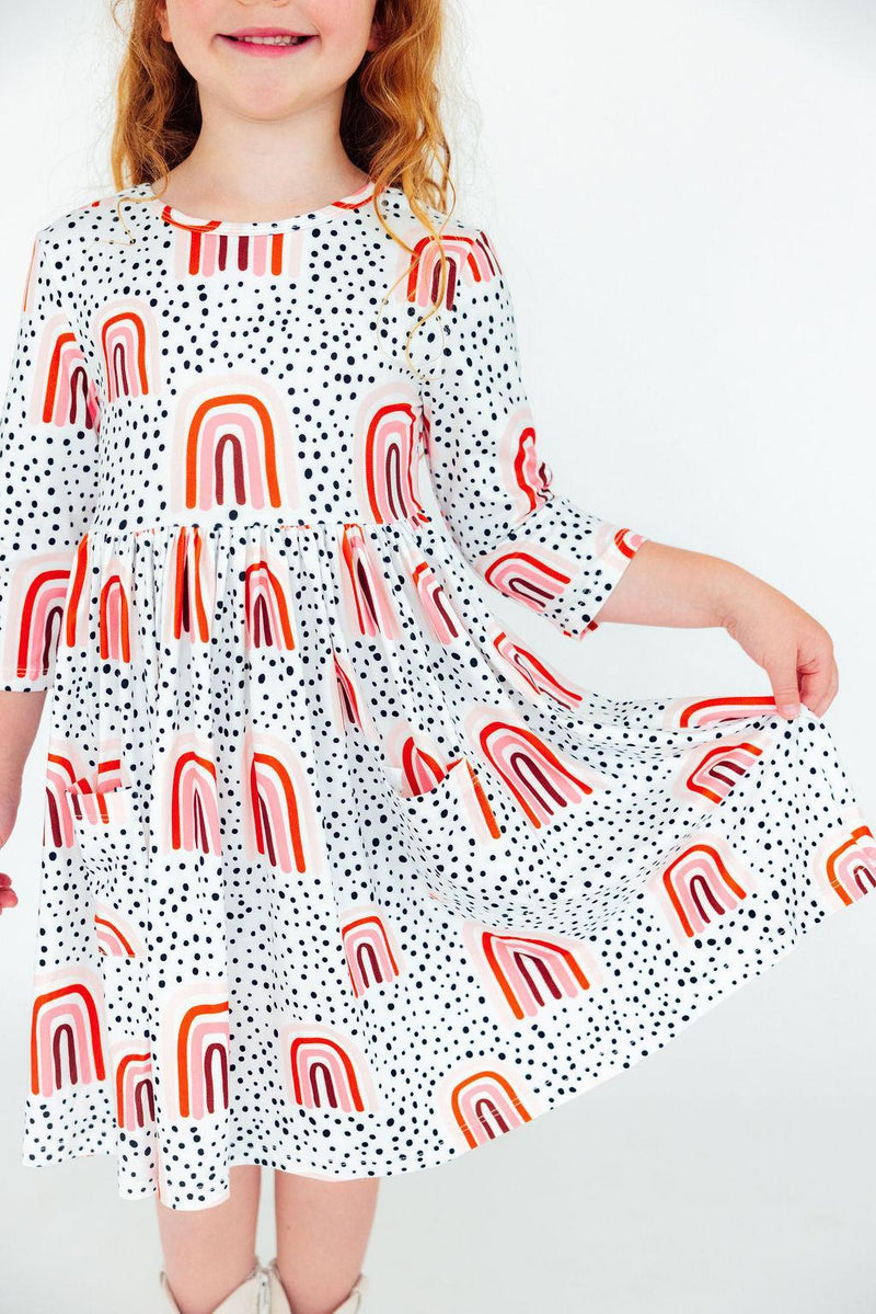 Close-up of a smiling girl displaying the playful design of the Peach Rainbow 3/4 Sleeve Pocket Twirl Dress, emphasizing its twirl-worthy skirt and vibrant prints.