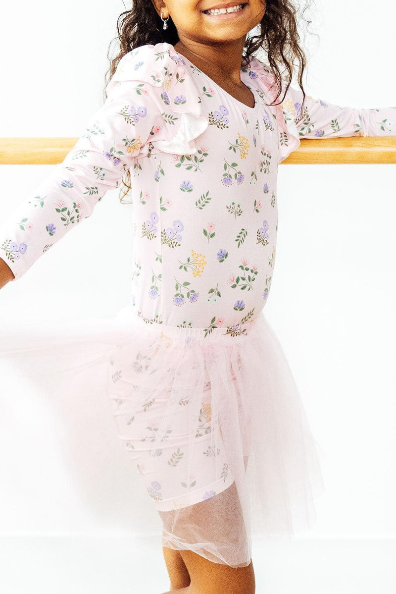 Little girl wearing the Pastel Petals Long Sleeve Flutter Leotard with a pink tutu, showcasing confidence and style in dance practice.