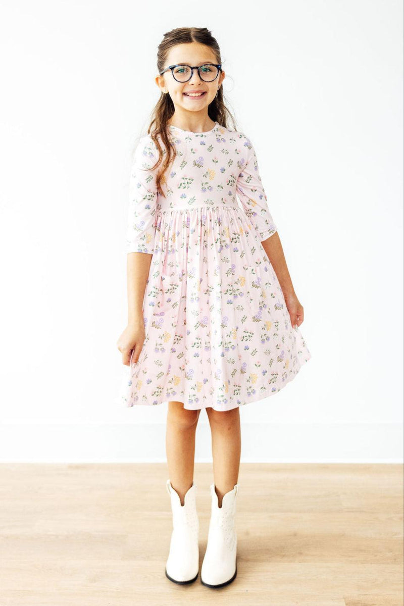 A happy girl in the Pastel Petals 3/4 Sleeve Pocket Twirl Dress, posing with confidence, her boots adding a trendy touch to this twirling delight.