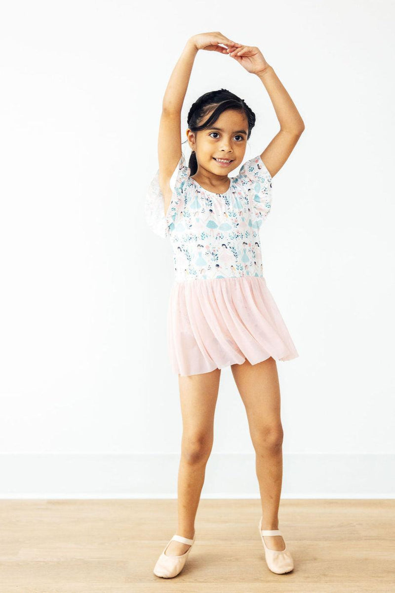 A young girl joyfully posing in a Twinkle Toes S/S Twirl Leotard, showcasing the playful design and pink tulle skirt, ideal for dance and play.