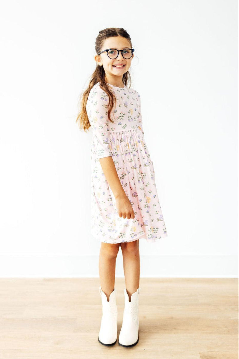 Adorable girl wearing the Pastel Petals 3/4 Sleeve Pocket Twirl Dress, showcasing its soft floral pattern, perfect for twirling and fun adventures. Complete with stylish glasses and cowboy boots for a playful look!