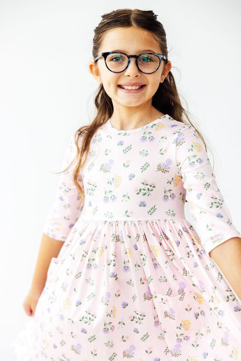 Smiling girl wearing the Pastel Petals 3/4 Sleeve Pocket Twirl Dress, showing off her playful side with a bright smile and charming details of the dress.