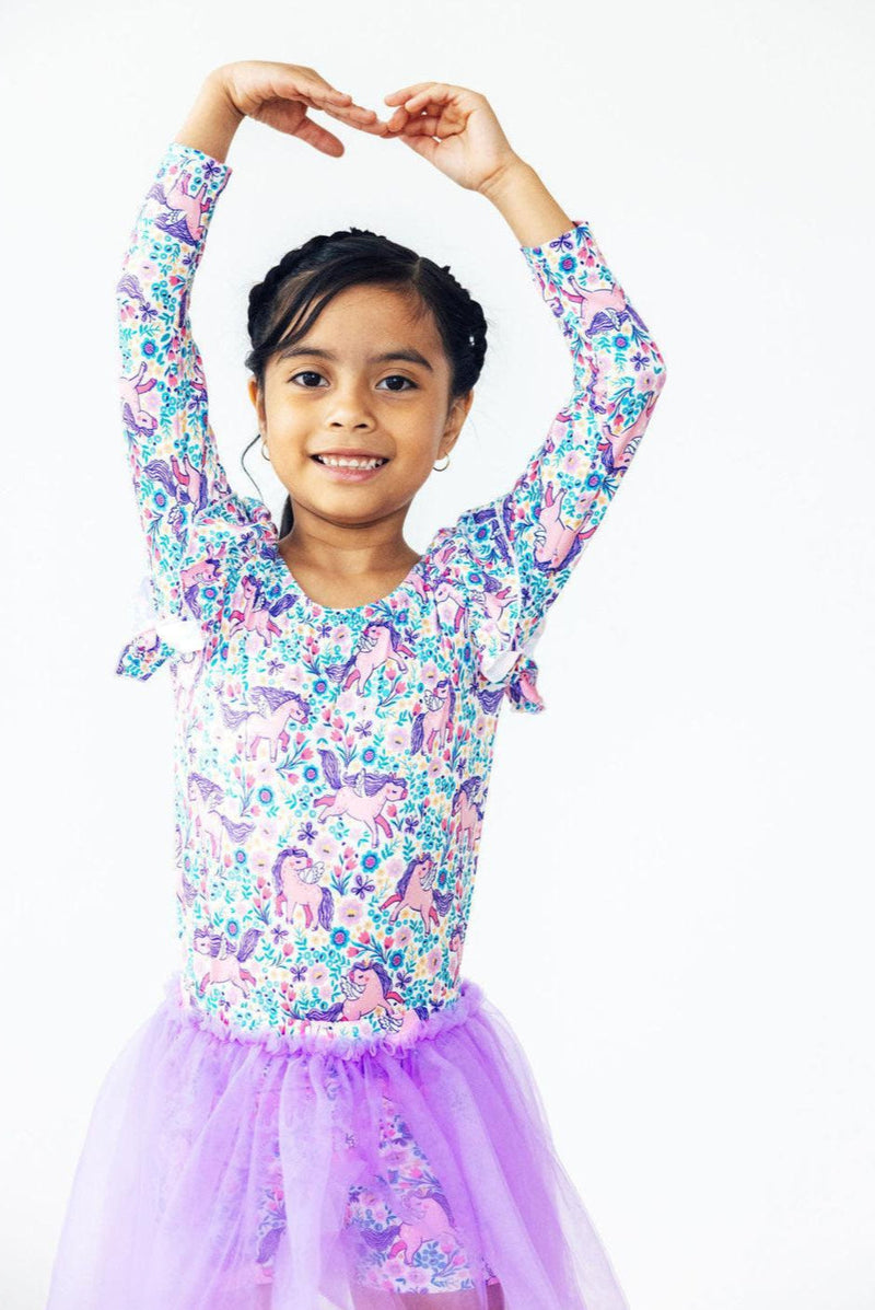 A cheerful girl wearing the Head in the Clouds Tutu Shorts, striking a ballet pose with arms raised, showcasing the playful and whimsical design perfect for little dancers.