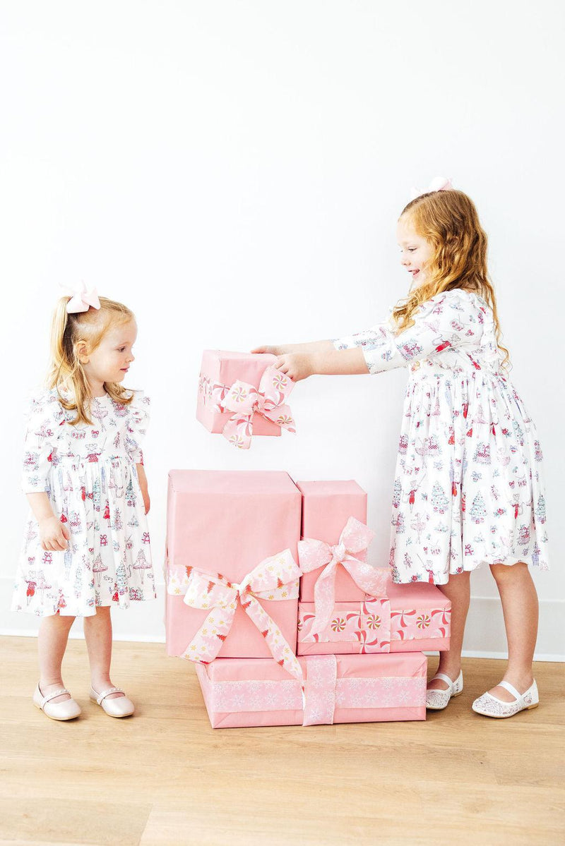 Two girls in Clara's Christmas 3/4 Sleeve Ruffle Twirl Dresses from Mila & Rose® joyfully interacting while surrounded by pink gift boxes.