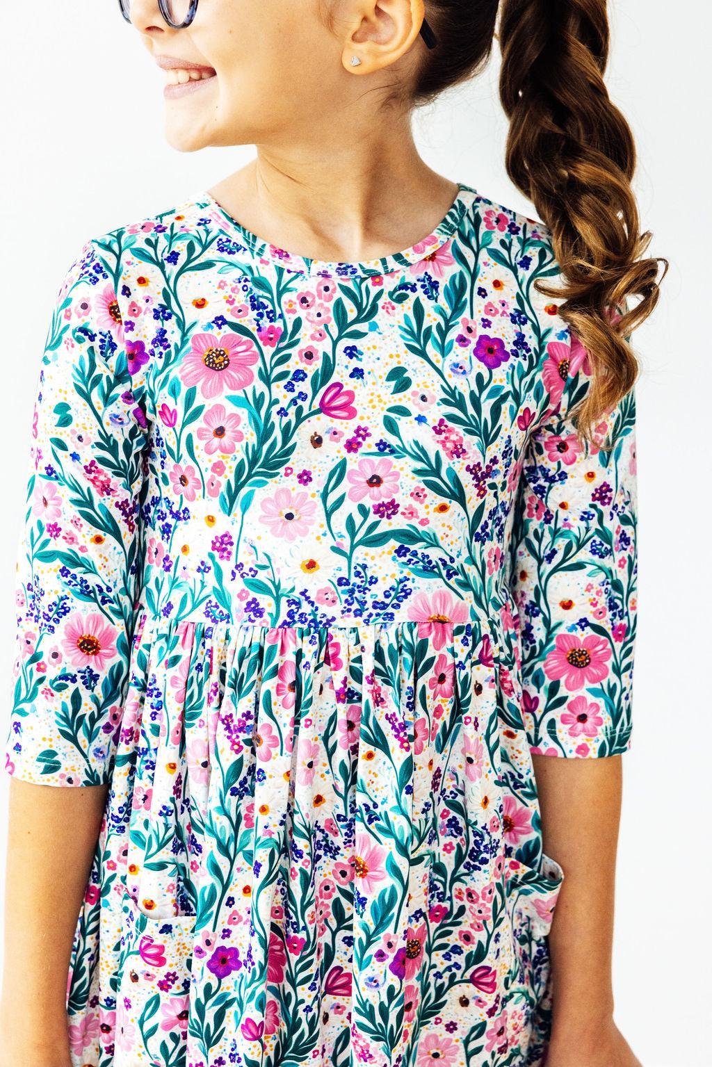 Close-up of a girl smiling while wearing the Vivid Garden 3/4 Sleeve Pocket Twirl Dress from Mila & Rose ®, showcasing the colorful floral design.