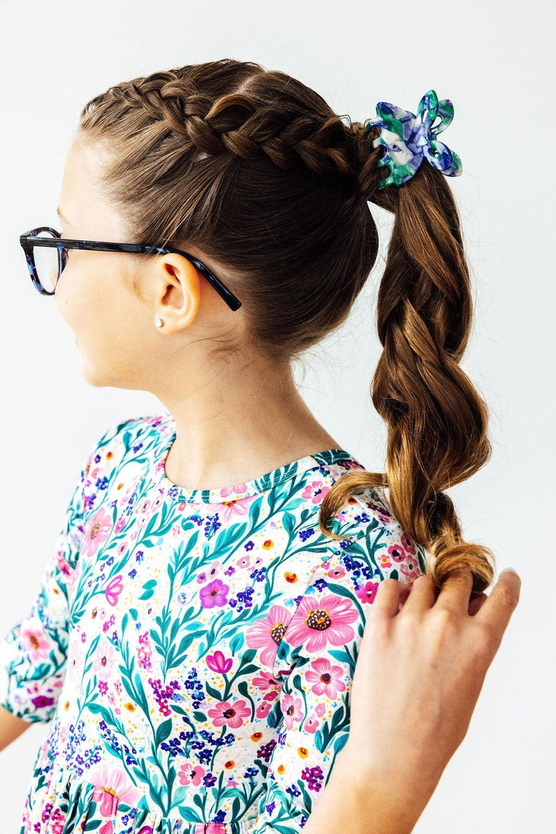 Side view of a girl in the Vivid Garden 3/4 Sleeve Pocket Twirl Dress from Mila & Rose ®, highlighting her braided hairstyle and the dress's lovely floral details.