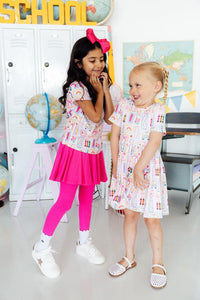 Two girls wearing Art Class Short Sleeve Pocket Twirl Dress twirl in a bright classroom with lockers.