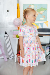 Girl wearing Art Class Short Sleeve Pocket Twirl Dress with a twirl skirt in a classroom.
