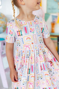 Girl wearing Art Class Short Sleeve Pocket Twirl Dress with full twirl skirt in bright classroom setting.