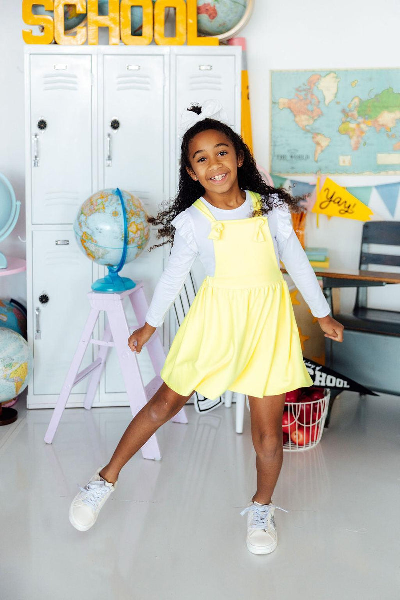 Smiling girl wearing a bright yellow faux suede pinafore in a classroom.
