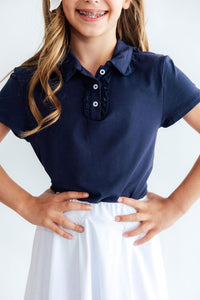 Girls navy ruffle polo with short sleeves and white buttons, featuring a feminine ruffle placket for polished school style.