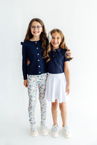 Girls navy ruffle polo paired with white skirt. Classic short sleeve shirt features feminine ruffle detail for polished school style.