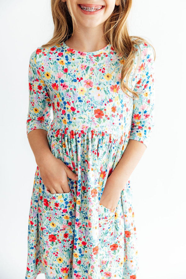 Girl wearing colorful floral 3/4 sleeve twirl dress with front pockets, designed for comfort and easy play.