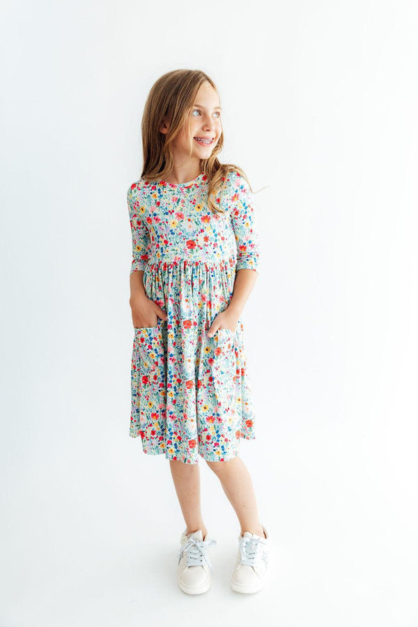 Girl wearing floral 3/4 sleeve twirl dress with side pockets, featuring comfortable fit and colorful print for school or play.