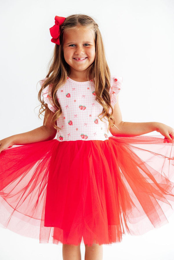 Young girl wearing a white top with red floral patterns and a red tutu skirt on a white background
