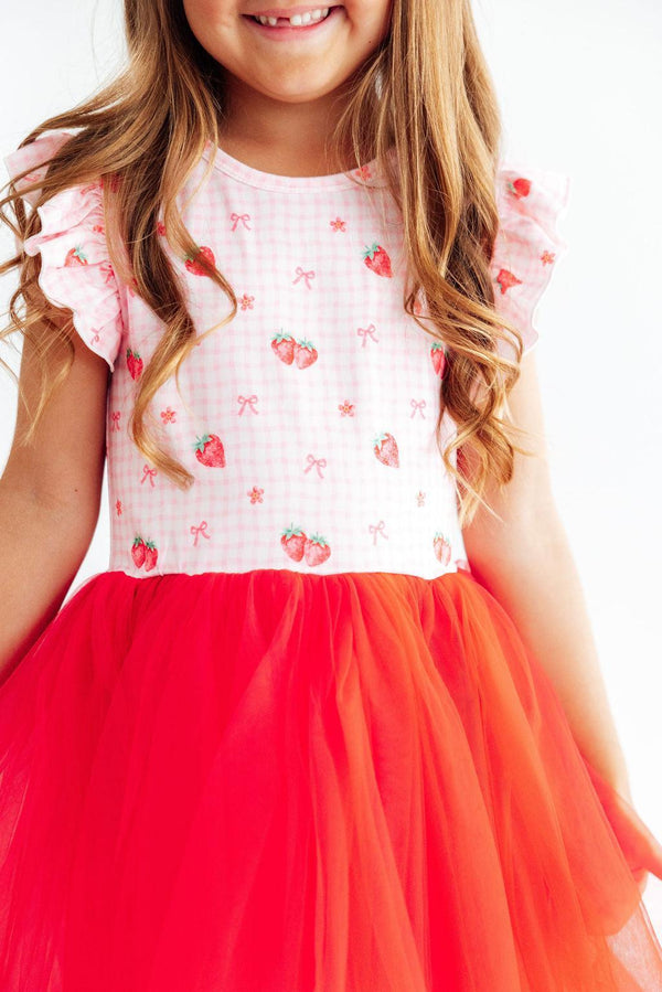 Young girl wearing a dress with strawberry pattern and red tulle skirt.