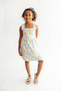 Girl wearing pastel Tropical Summer Ruffle Cross Back Dress with crisscross back straps and ruffled shoulders.