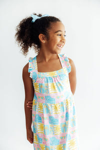 Girl wearing pastel tropical print dress with ruffle straps and crisscross back.