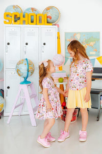 Two girls in Playground Princess Short Sleeve Pocket Twirl Dress twirl in a playroom with lockers and globes.