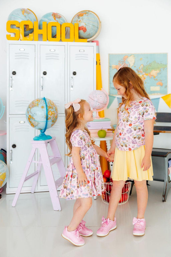 Two girls in Playground Princess Short Sleeve Pocket Twirl Dress twirl in a playroom with lockers and globes.
