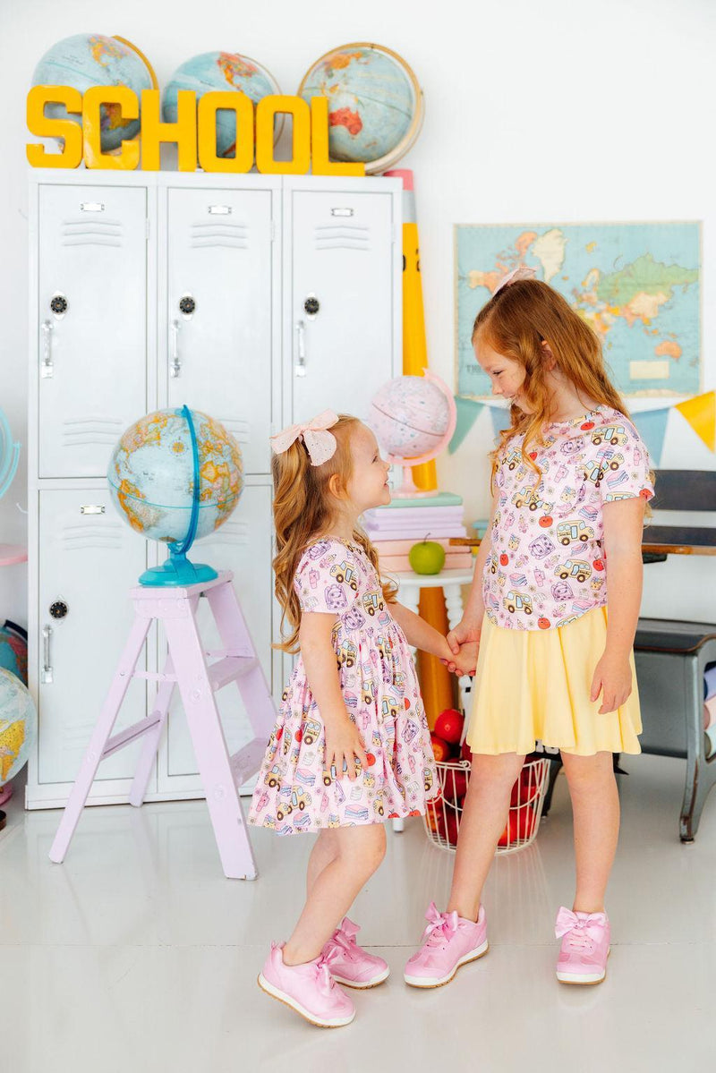 Two girls in Playground Princess Short Sleeve Pocket Twirl Dress twirl in a playroom with lockers and globes.