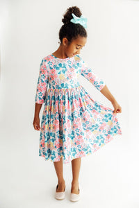 Girl wearing Floral Garden 3/4 sleeve twirl dress in pink and blue floral print with mint hair bow.