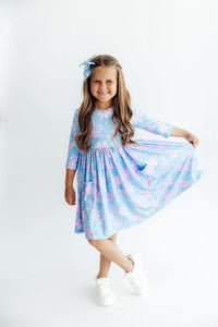 Girl twirling in blue and pink floral 3/4 sleeve pocket dress with full skirt, scoop back, and ballet neckline for play.