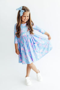 Girl twirling in blue floral 3/4 sleeve pocket dress with full skirt and matching bow headband. Perfect for school or play.