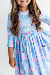 Child wearing blue and pink floral 3/4 sleeve twirl dress with side pockets and full skirt for play.
