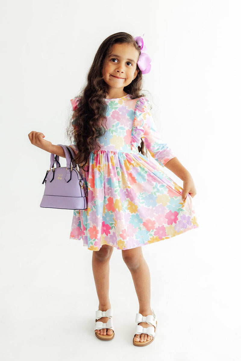 Girl in colorful carnations 3/4 sleeve ruffle twirl dress with a full-circle skirt, holding a lavender bag.