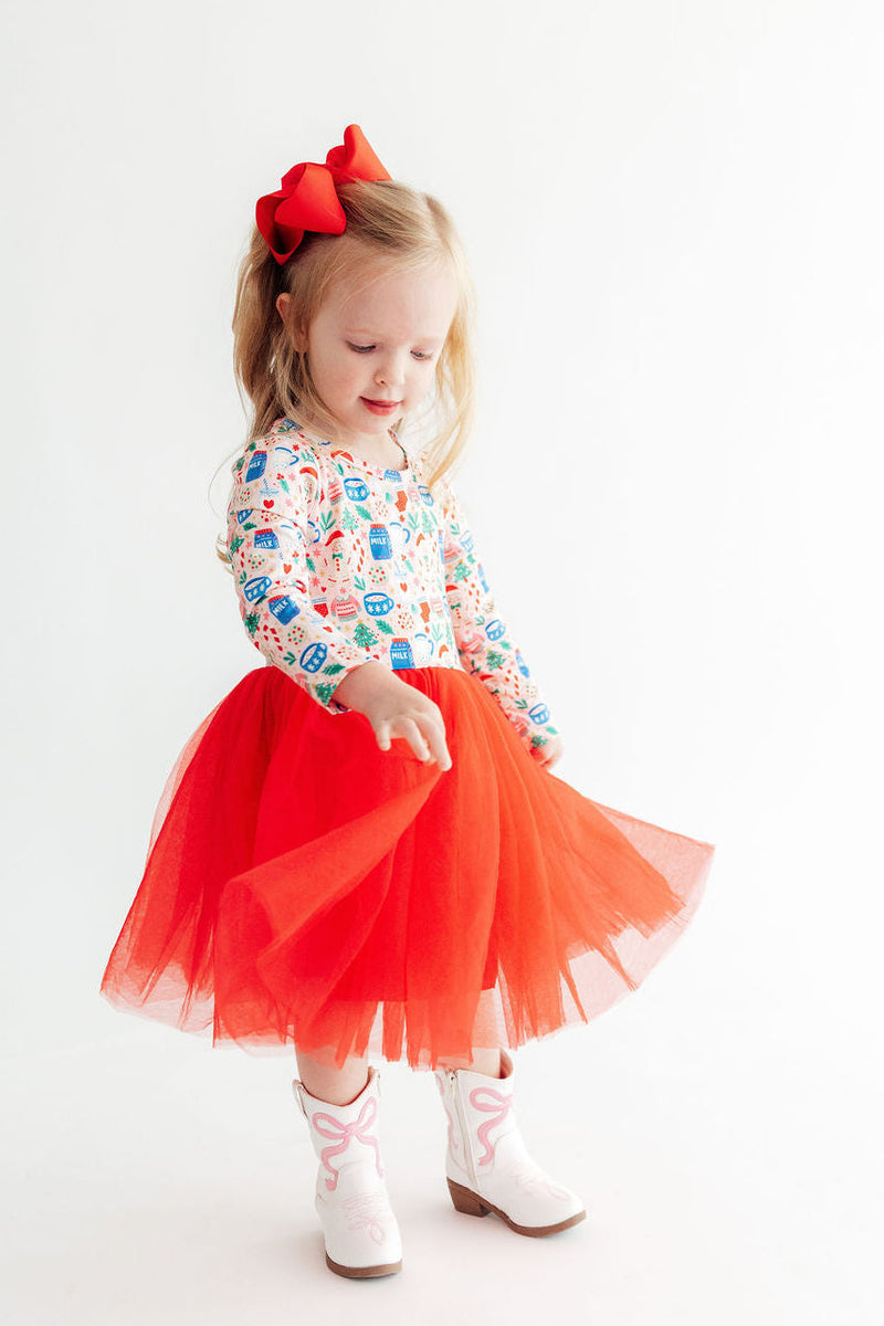 Toddler girl twirling in red long sleeve tutu dress with holiday print top, red bow, and white cowboy boots.