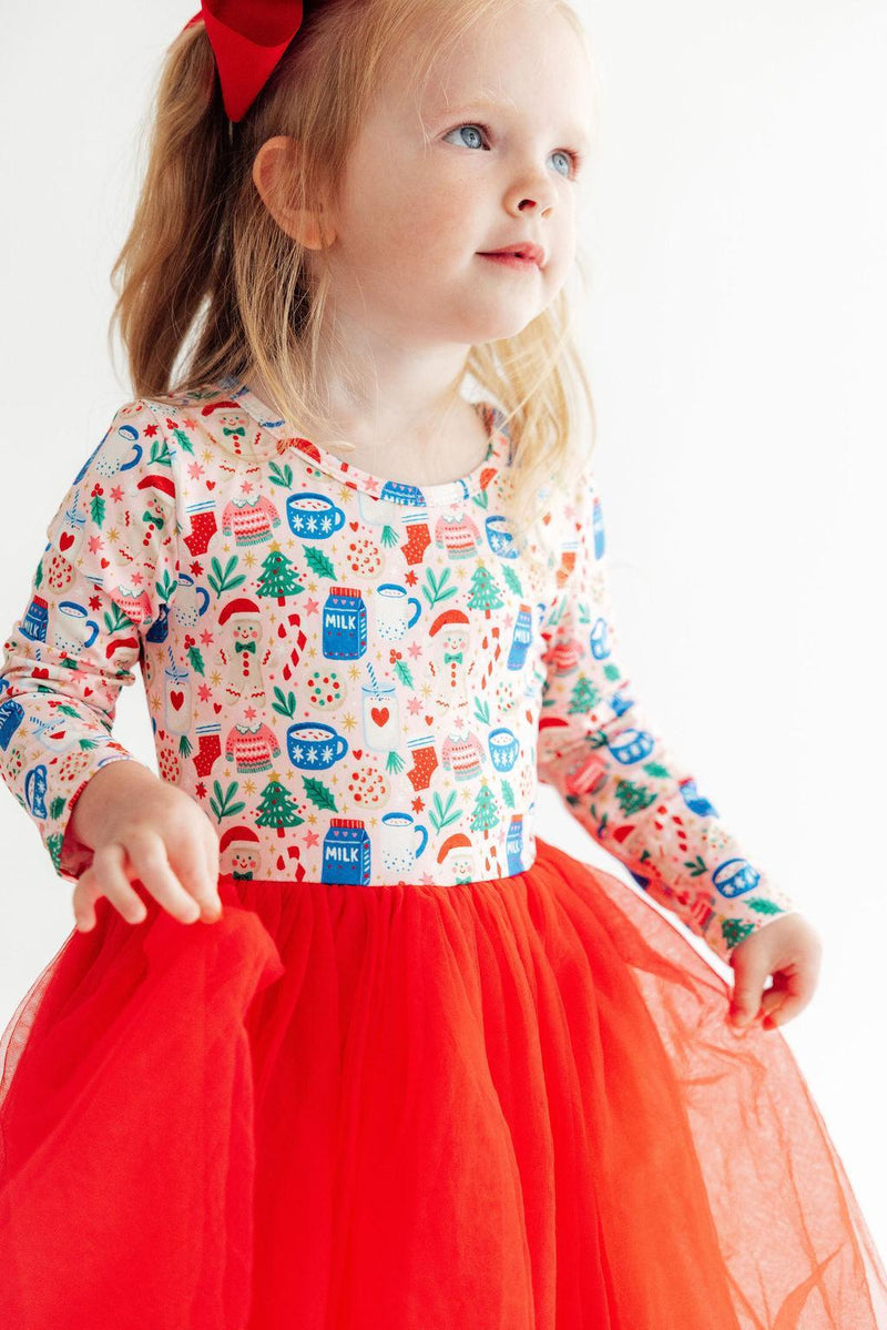 Toddler girl wearing a long sleeve holiday print dress with a bright red tulle tutu skirt and red bow in hair.