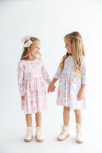 Two girls wearing Here for the Candy 3/4 sleeve pocket twirl dresses in pastel stripes, holding hands and smiling.
